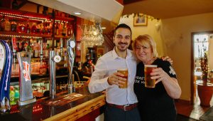 two people pose with pints of beer infront of a bar