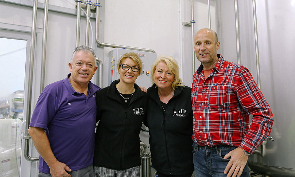 Dave joins the team with other team member smiling for a photograph inside a brewery